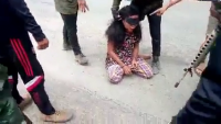 Several Men Beat A Woman Kneeling In The Middle Of The Road